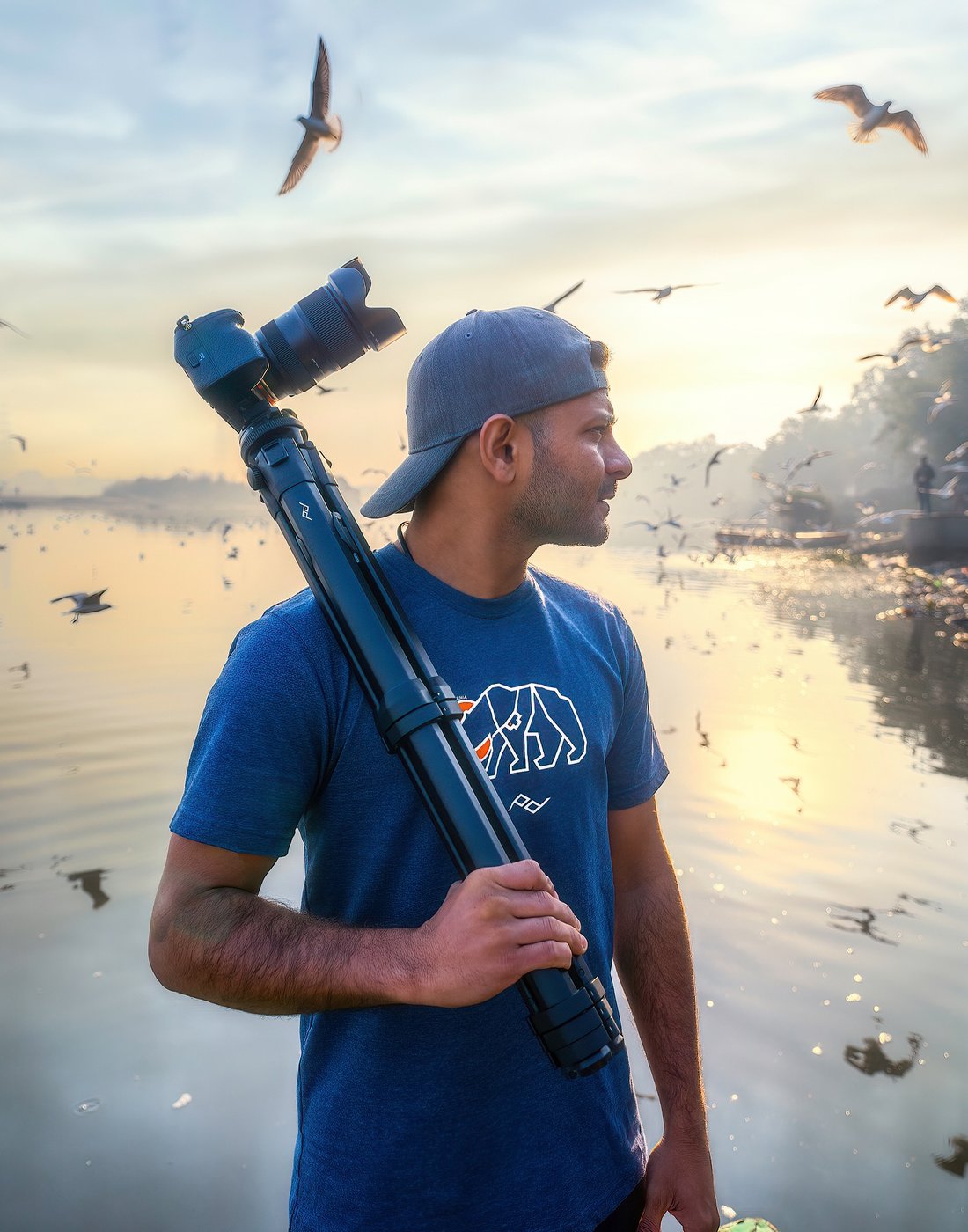 Ashik Aseem with camera and tripod, birds rising off the backwaters at dawn