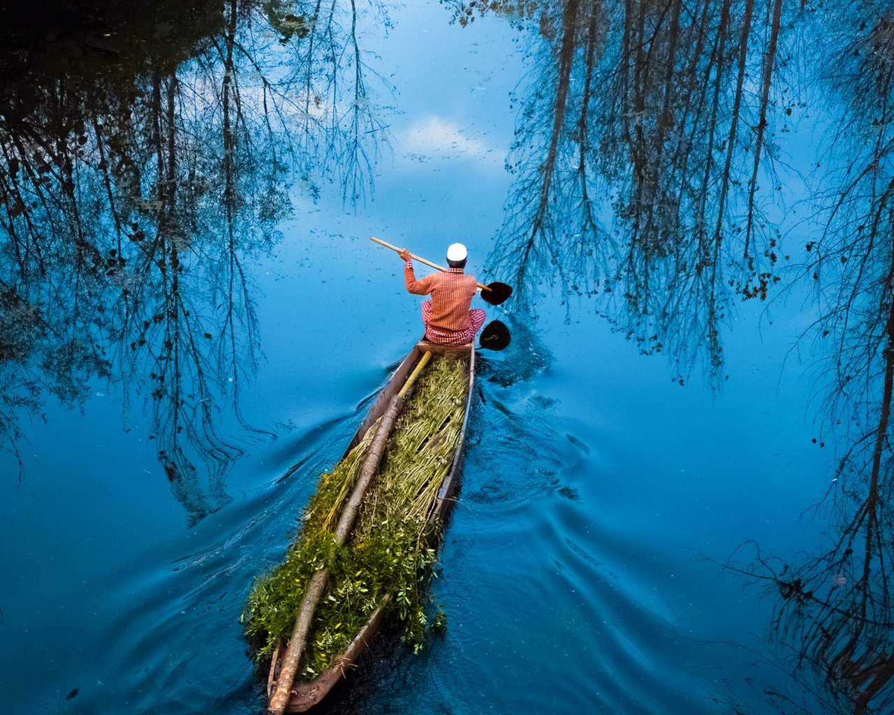 Aerial of a lone boatman on a mirror-blue Kashmir waterway