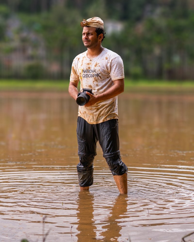 Ashik standing waist-deep in the backwaters with his camera at dawn